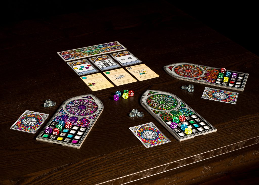 Photo showing a game of Sagrada in progress. Three boards in the shape of stained-glass cathedral windows are being covered in multicoloured dice. 